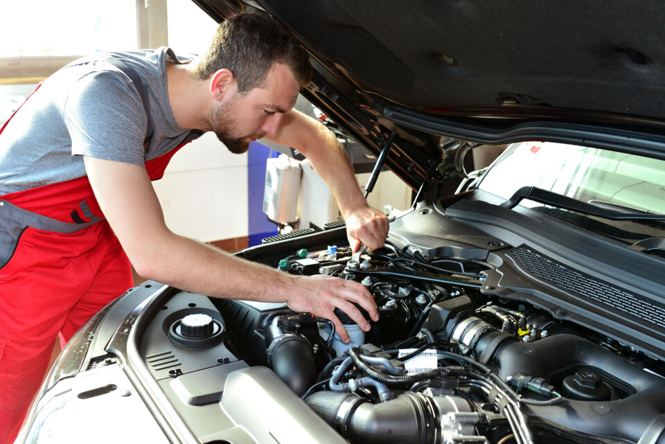 KFZ Mechaniker Repariert Motor Eines Fahrzeugs In Der Autowerkstatt Car Mechanic Repairs Engine Of A Vehicle In The Garage (1)