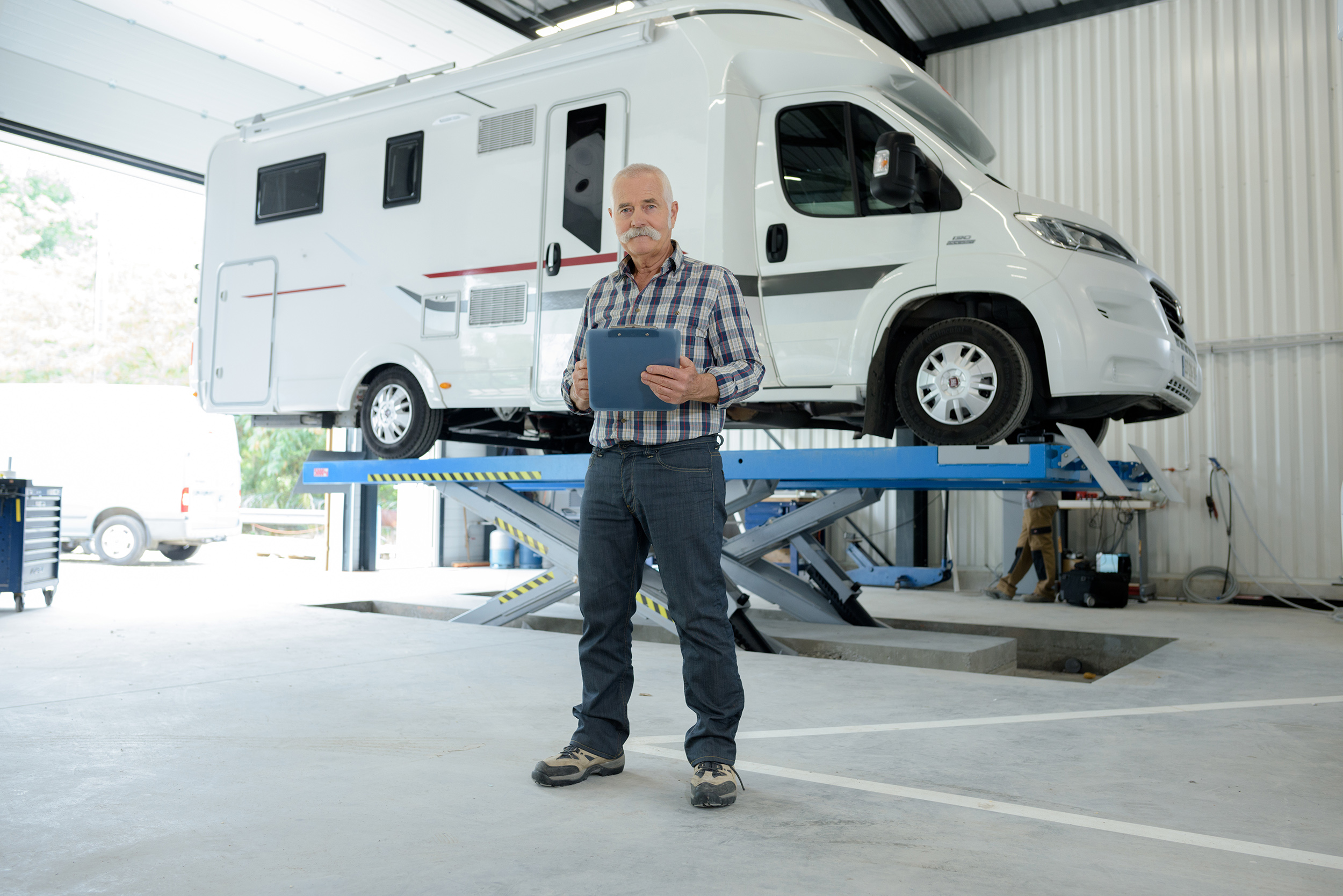 Werkstatt-Mitarbeiter steht vor einem Wohnmobil in der Werkstatt